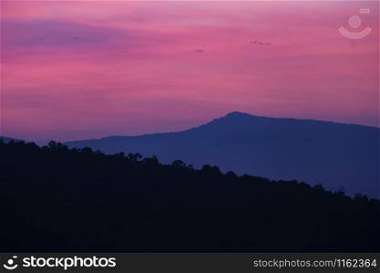 Nature landscape background beautiful view of the morning fog filling the valleys of smooth hills mountain range layer dark blue forest sunrise and sunset in mountains with purple sky dramatic