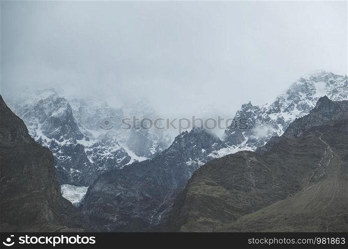 Nature landscape view of clouds and fog covered snow capped Ultar Sar mountain in Karakoram range, Hunza valley. Gilgit Baltistan, Pakistan.