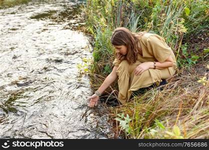 nature, occult science and supernatural concept - young woman or witch performing magic ritual on river and touching water. woman or witch performing magic ritual on river
