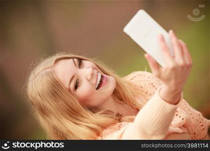 Nature outdoor internet technology concept. Cheerful blonde girl taking selfie. Young gorgeous lady takes picture of herself in autumnal forest.. Cheerful blonde girl taking selfie.
