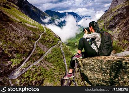Nature photographer tourist with camera shoots while standing on top of the mountain. Troll&rsquo;s Path Trollstigen or Trollstigveien winding mountain road in Norway.