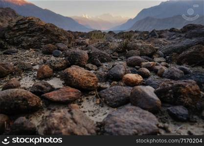 Nature rough landscape view of rocks stones boulders and pebbles against Karakoram mountain range in background. Sunset in Gilgit Baltistan, Pakistan. Selective focus.
