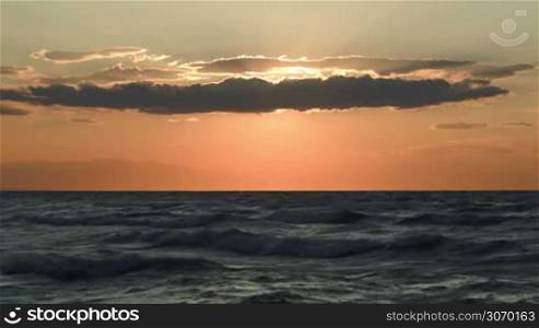 Nature scene of rough wavy sea and evening sun hidden with heavy cloud