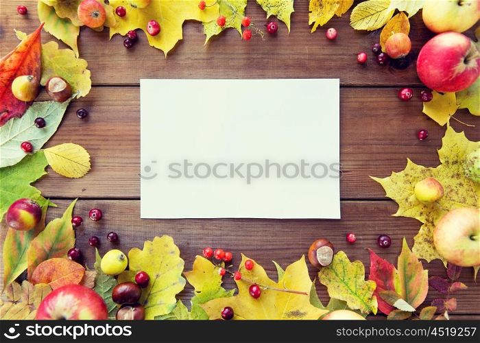 nature, season, advertisement and decor concept - close up of white paper sheet in frame of autumn leaves, fruits and berries on wooden table