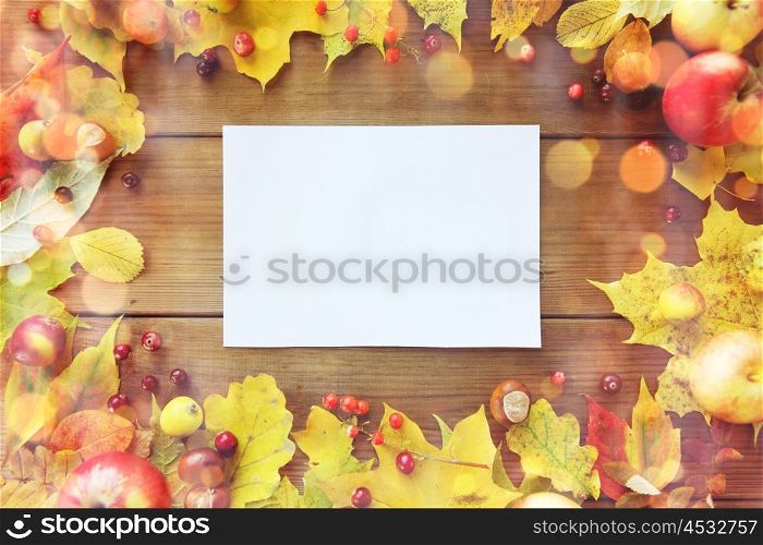nature, season, advertisement and decor concept - close up of white paper sheet in frame of autumn leaves, fruits and berries on wooden table
