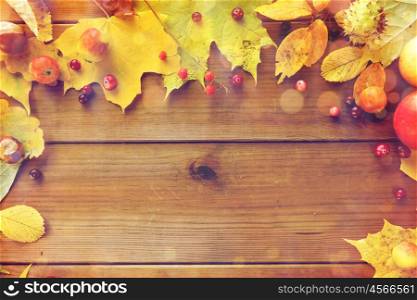 nature, season, advertisement and decor concept - frame of autumn leaves, fruits and berries on wooden table