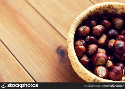 nature, season, autumn and botany concept - close up of chestnuts in wicker basket on wooden table