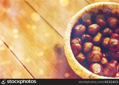 nature, season, autumn and botany concept - close up of chestnuts in wicker basket on wooden table