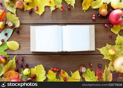 nature, season, inspiration and memories concept - close up of empty book or album in frame of autumn leaves, fruits and berries on wooden table