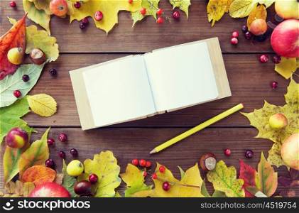 nature, season, inspiration and memories concept - close up of empty note book or album with pencil in frame of autumn leaves, fruits and berries on wooden table