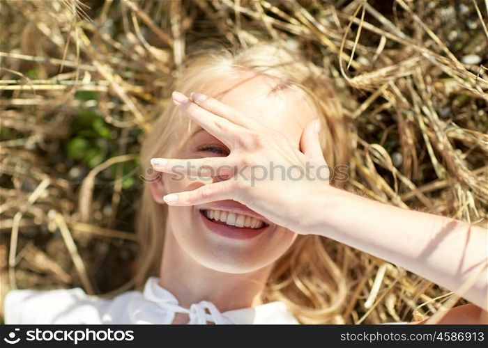 nature, summer holidays, vacation and people concept - close up of happy young woman lying on cereal field and covering face by hand