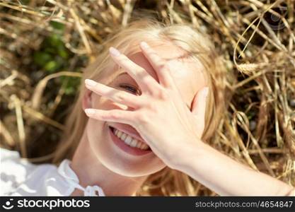 nature, summer holidays, vacation and people concept - close up of happy young woman lying on cereal field and covering face by hand