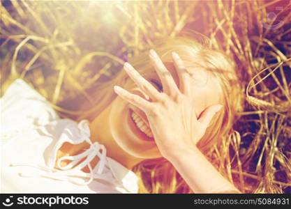nature, summer holidays, vacation and people concept - close up of happy young woman lying on cereal field and covering face by hand. happy young woman lying on cereal field. happy young woman lying on cereal field