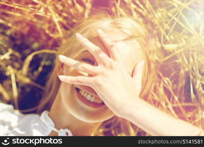 nature, summer holidays, vacation and people concept - close up of happy young woman lying on cereal field and covering face by hand. happy young woman lying on cereal field