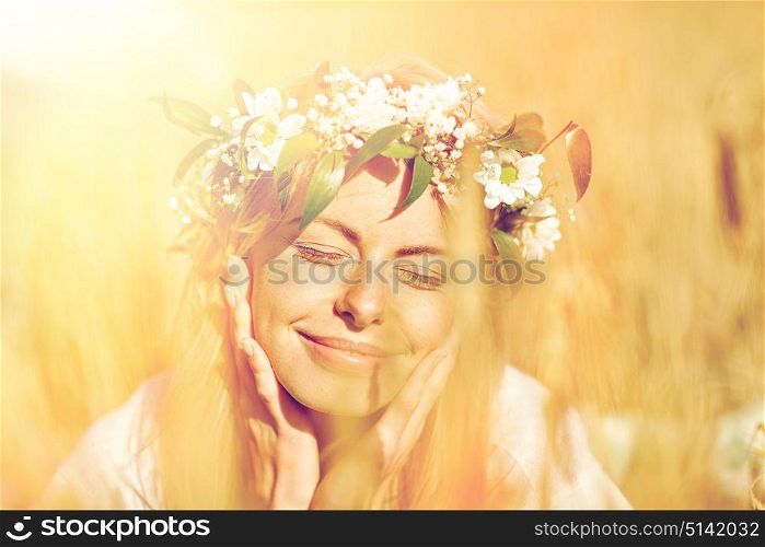 nature, summer holidays, vacation and people concept - face of happy smiling woman or teenage girl n in wreath of flowers on cereal field. happy woman in wreath of flowers on cereal field