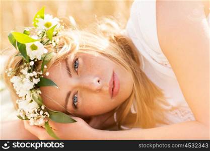 nature, summer holidays, vacation and people concept - face of happy woman in wreath of flowers lying on cereal field