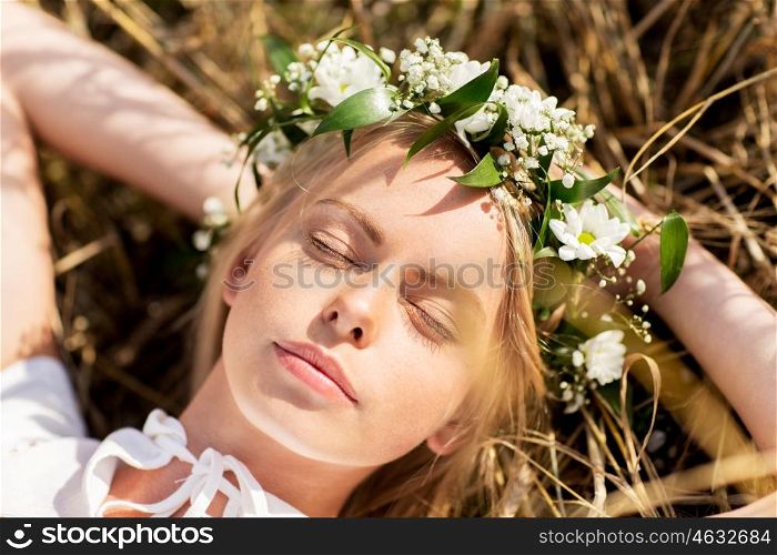 nature, summer holidays, vacation and people concept - happy smiling woman in wreath of flowers lying on straw