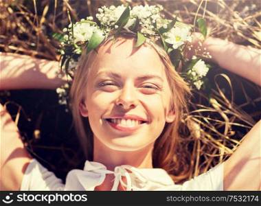 nature, summer holidays, vacation and people concept - happy smiling woman in wreath of flowers lying on straw. happy woman in wreath of flowers lying on straw