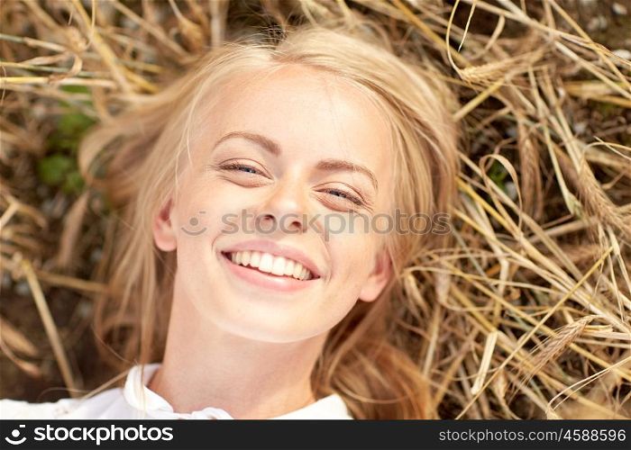 nature, summer holidays, vacation and people concept - happy smiling young woman or teenage girl lying and enjoying sun on cereal field