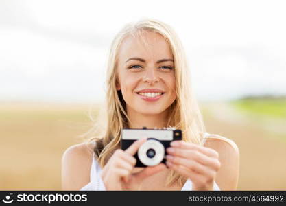 nature, summer holidays, vacation and people concept - happy smiling young woman with film camera outdoors