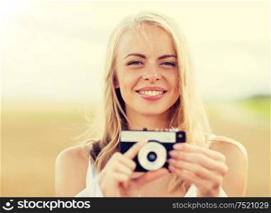 nature, summer holidays, vacation and people concept - happy smiling young woman with film camera outdoors. happy young woman with film camera outdoors