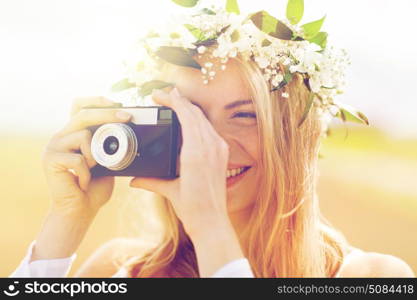 nature, summer holidays, vacation and people concept - happy woman in wreath of flowers taking picture with film camera outdoors. happy woman with film camera in wreath of flowers. happy woman with film camera in wreath of flowers