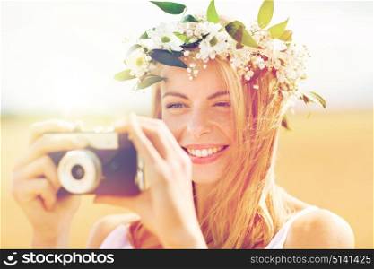 nature, summer holidays, vacation and people concept - happy woman in wreath of flowers taking picture with film camera outdoors. happy woman with film camera in wreath of flowers