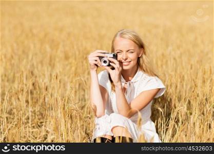 nature, summer holidays, vacation and people concept - happy woman taking picture with film camera outdoors