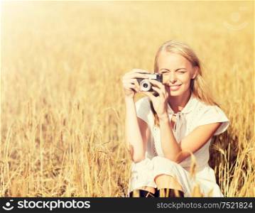 nature, summer holidays, vacation and people concept - happy woman taking picture with film camera outdoors. happy woman with film camera in wreath of flowers