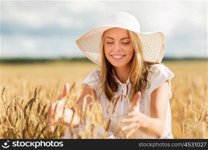 nature, summer holidays, vacation and people concept - happy young woman in white dress and sun hat enjoying sun on cereal field