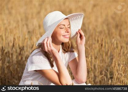 nature, summer holidays, vacation and people concept - happy young woman in white dress and sun hat enjoying sun on cereal field