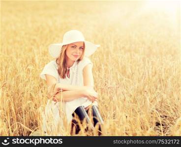 nature, summer holidays, vacation and people concept - happy young woman in white dress, rubber boots and sun hat sitting on cereal field. happy young woman in sun hat on cereal field