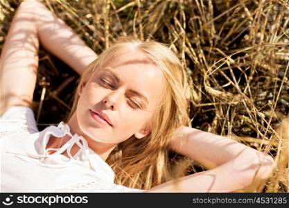nature, summer holidays, vacation and people concept - happy young woman lying and enjoying sun on cereal field or hay