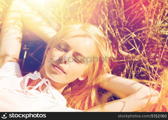 nature, summer holidays, vacation and people concept - happy young woman lying and enjoying sun on cereal field or hay. happy young woman lying on cereal field or hay