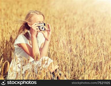 nature, summer holidays, vacation and people concept - happy young woman taking picture with vintage film camera in cereal field. woman taking picture with camera in cereal field