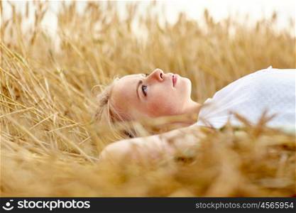 nature, summer holidays, vacation and people concept - young woman or teenage girl lying and dreaming on cereal field