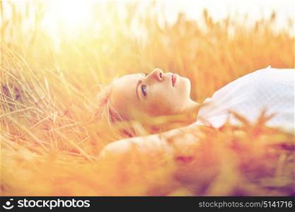 nature, summer holidays, vacation and people concept - young woman or teenage girl lying and dreaming on cereal field. young woman lying on cereal field and dreaming