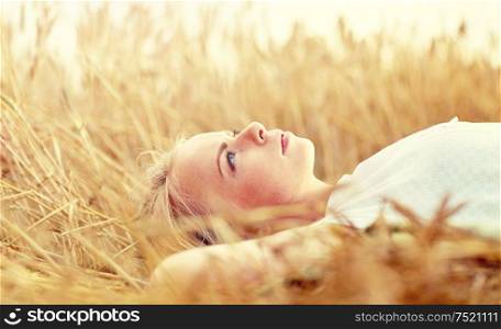 nature, summer holidays, vacation and people concept - young woman or teenage girl lying and dreaming on cereal field. young woman lying on cereal field and dreaming