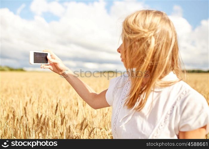 nature, summer vacation, technology and people concept - close up of young woman with smartphone taking picture of cereal field