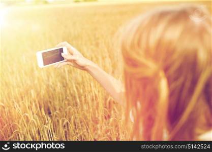 nature, summer vacation, technology and people concept - close up of young woman with smartphone taking picture of cereal field. close up of girl with smartphone on cereal field