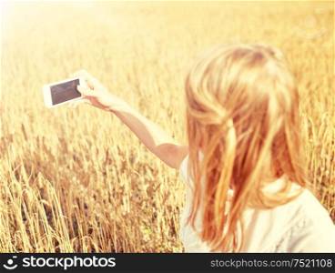 nature, summer vacation, technology and people concept - close up of young woman with smartphone taking picture of cereal field. close up of girl with smartphone on cereal field