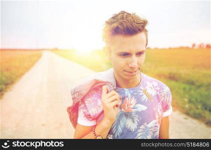 nature, summer, youth culture and people concept - sad young hippie man walking along country road chewing rye spike. sad young hippie man walking along country road