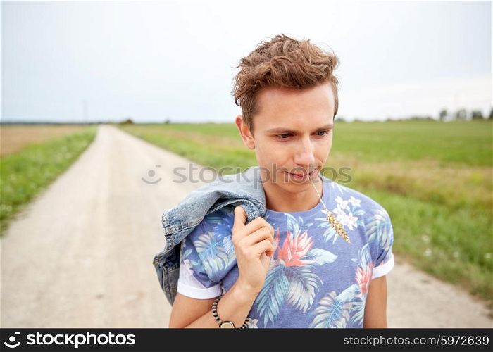 nature, summer, youth culture and people concept - sad young hippie man walking along country road chewing rye spike