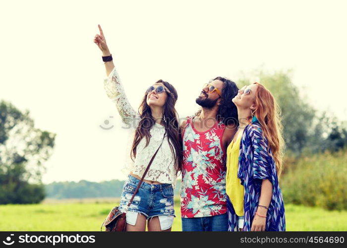 nature, summer, youth culture and people concept - smiling young hippie friends in sunglasses pointing finger up outdoors
