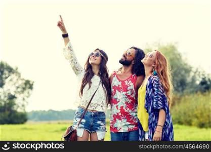 nature, summer, youth culture and people concept - smiling young hippie friends in sunglasses pointing finger up outdoors