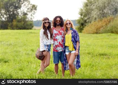 nature, summer, youth culture and people concept - smiling young hippie friends in sunglasses on green field