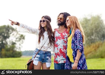 nature, summer, youth culture and people concept - smiling young hippie friends in sunglasses pointing finger to something on green field