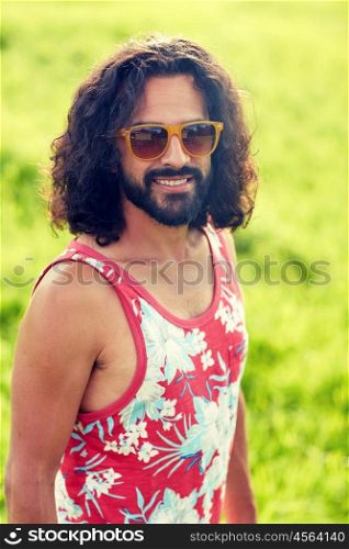 nature, summer, youth culture and people concept - smiling young hippie man in sunglasses on green field