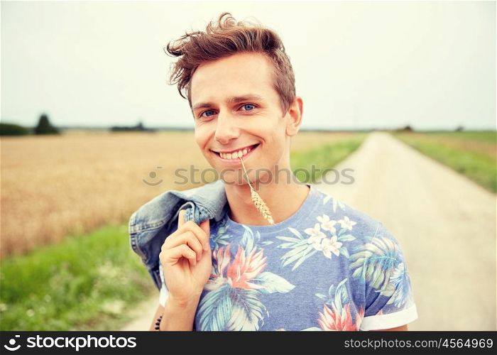 nature, summer, youth culture and people concept - smiling young hippie man on country road chewing rye spike