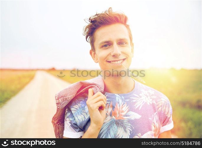 nature, summer, youth culture and people concept - smiling young hippie man on country road chewing rye spike. smiling young hippie man on country road